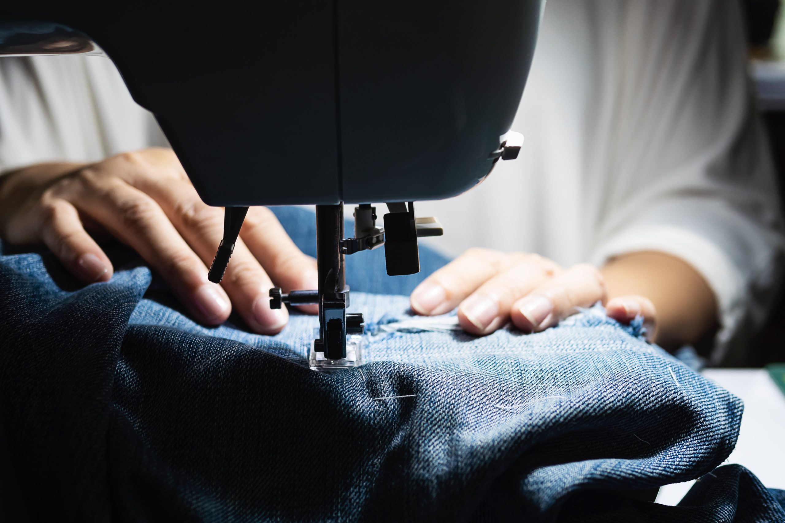 Woman doing jeans patchwork using sewing machine - home DIY sewing concept